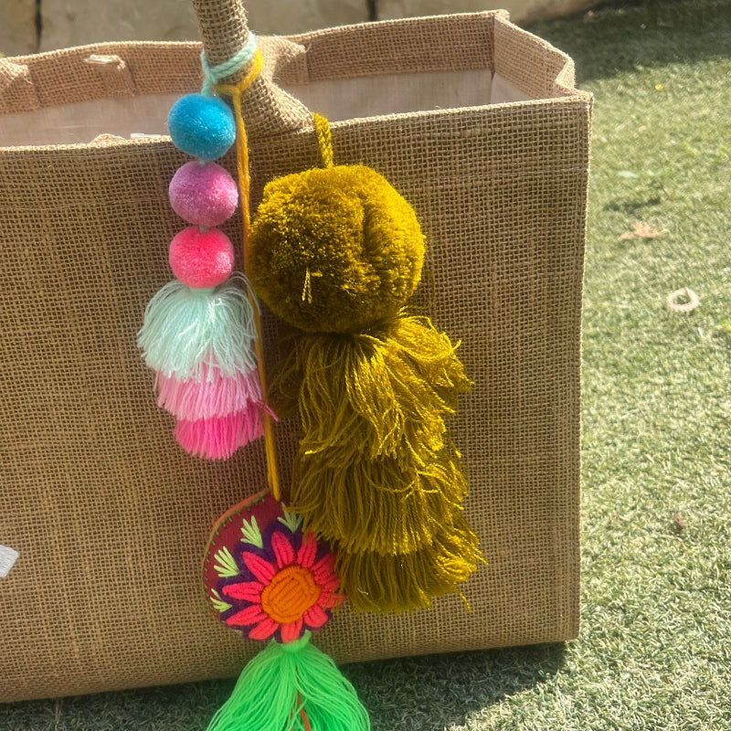 Mustard yellow fluffy tassel keychain with soft pom pom placed on grass background