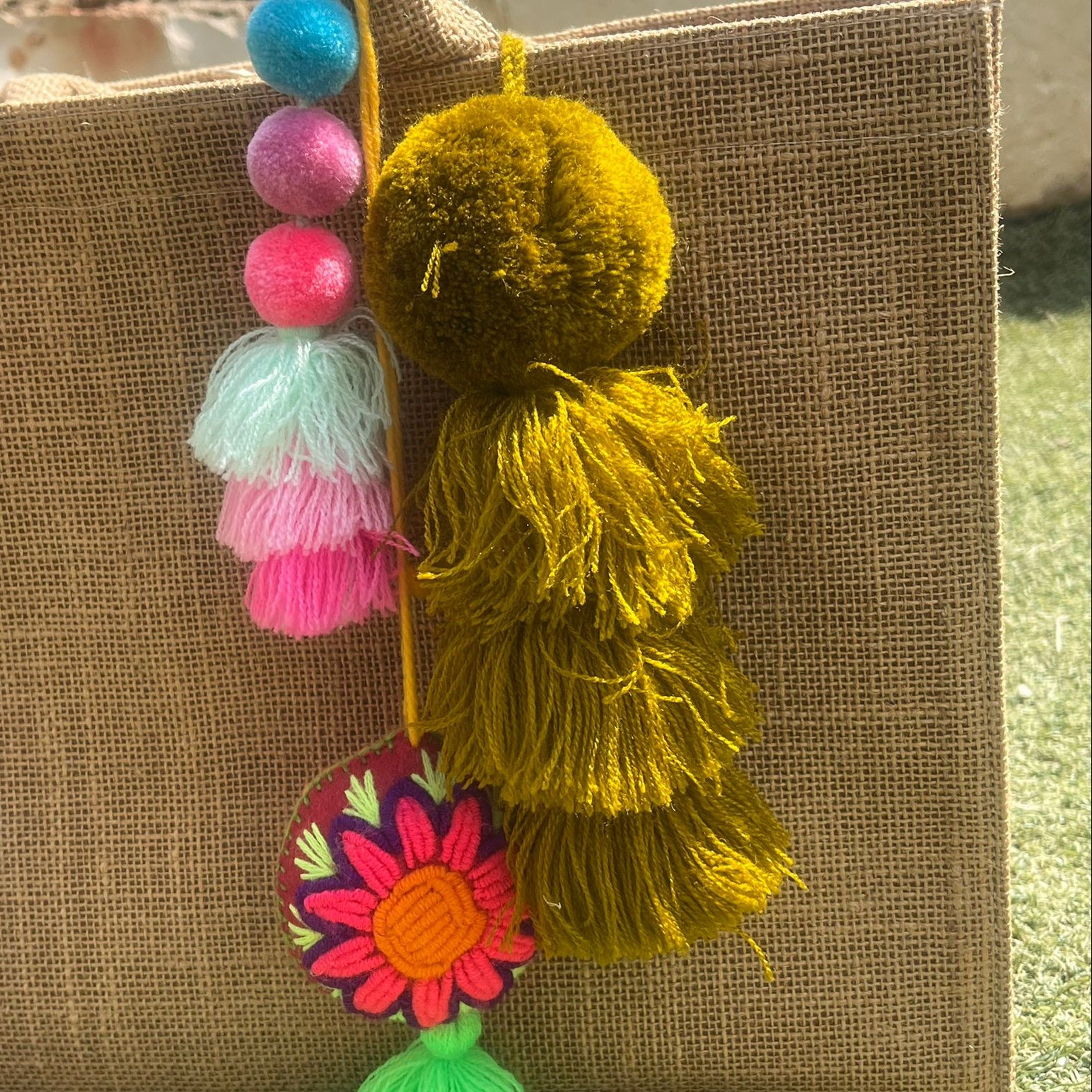 Mustard yellow fluffy tassel keychain with soft pom pom placed on grass background