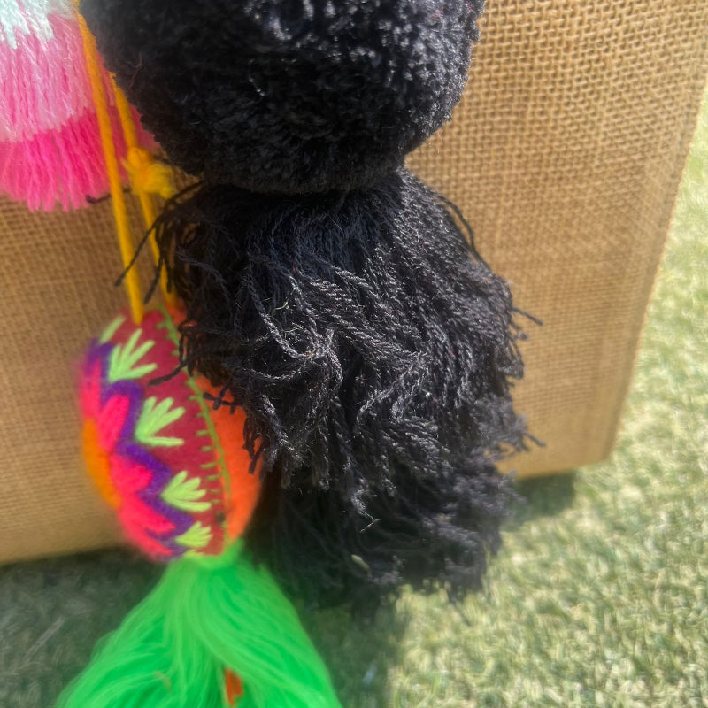 Black fluffy tassel keychain with soft pom pom placed on grass background