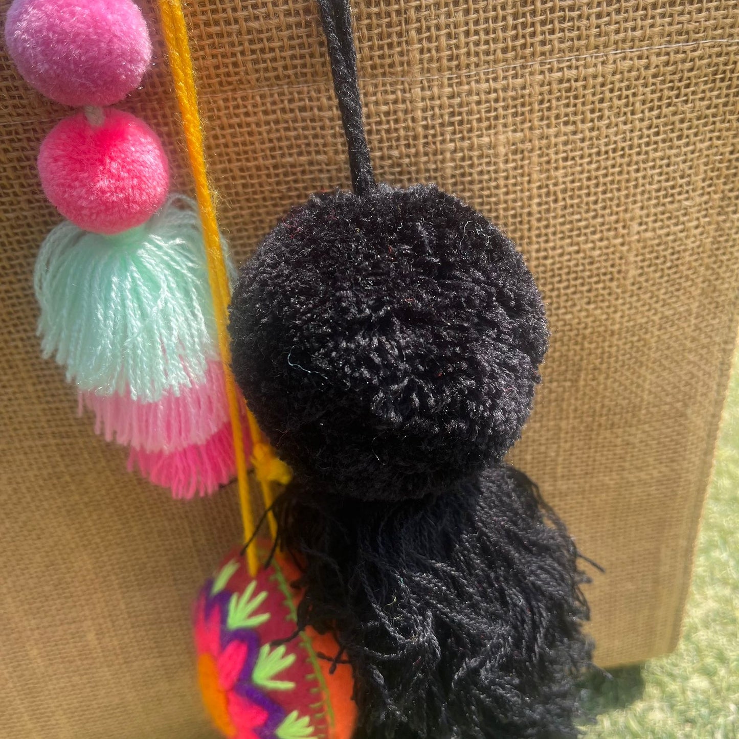 Black fluffy tassel keychain with soft pom pom placed on grass background