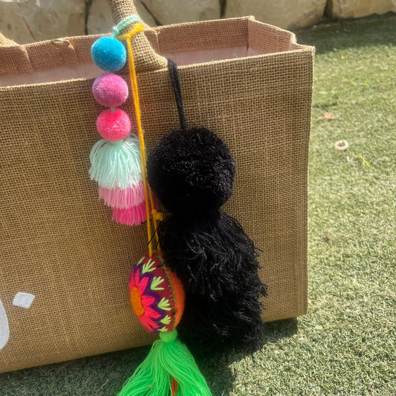 Black fluffy tassel keychain with soft pom pom placed on grass background