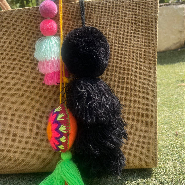 Black fluffy tassel keychain with soft pom pom placed on grass background