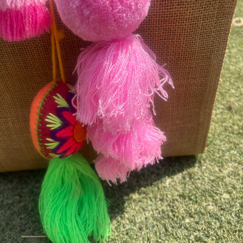 Pink fluffy tassel keychain with soft pom pom placed on grass background