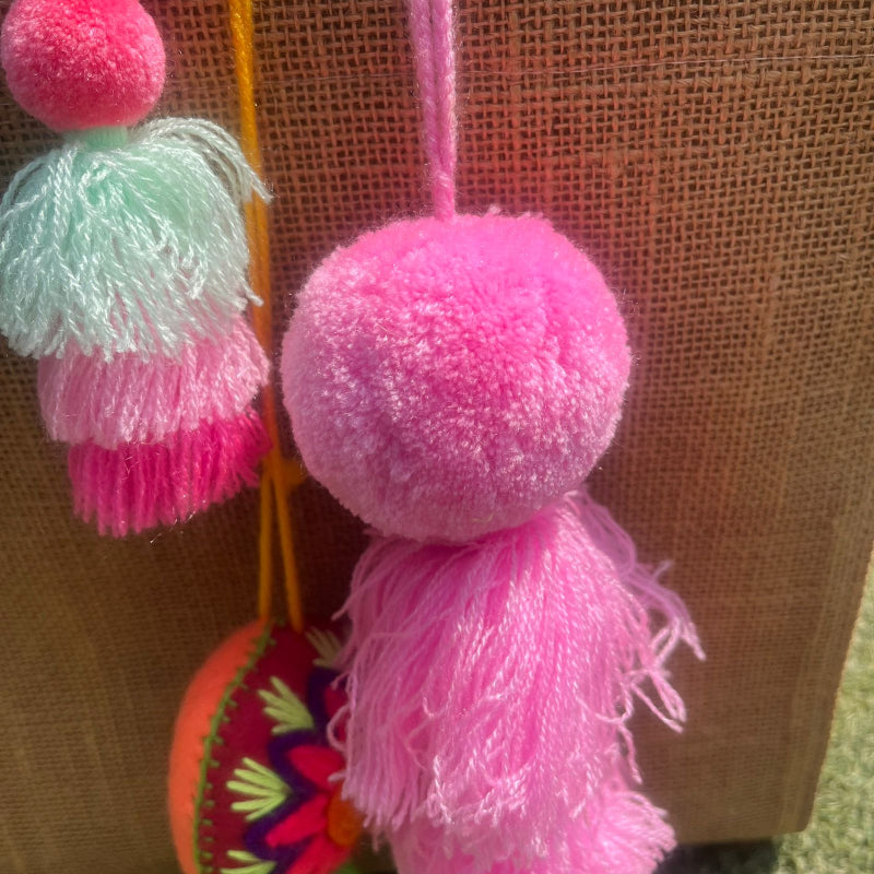 Pink fluffy tassel keychain with soft pom pom placed on grass background