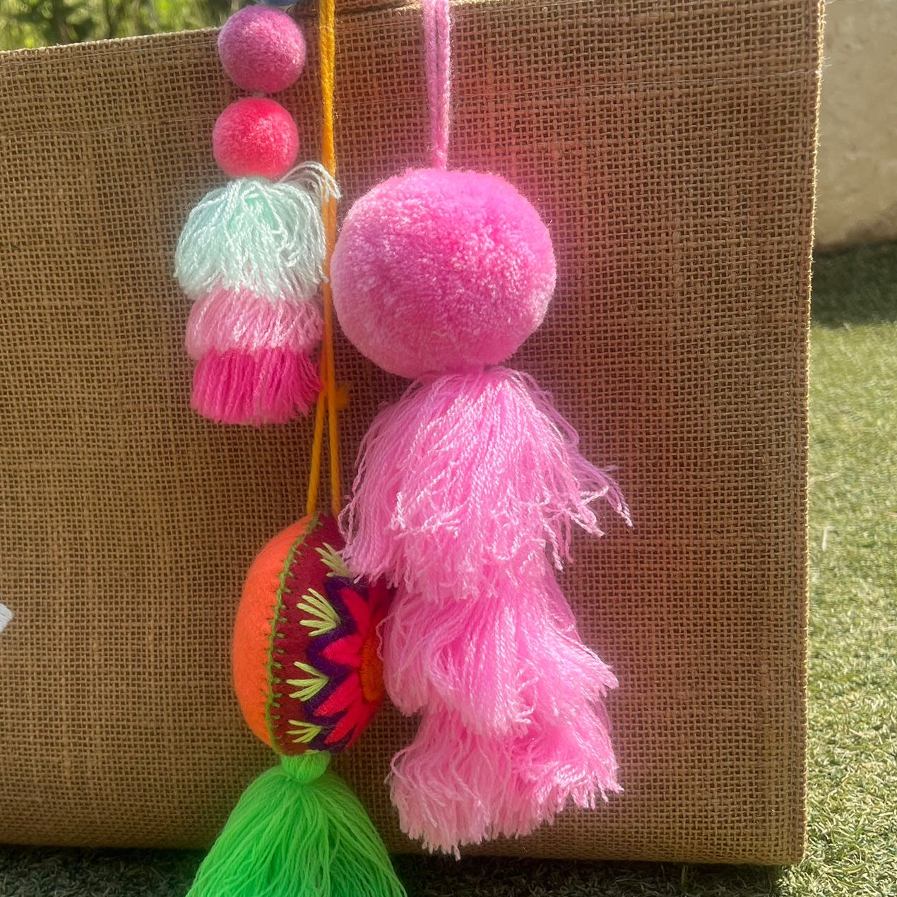 Pink fluffy tassel keychain with soft pom pom placed on grass background