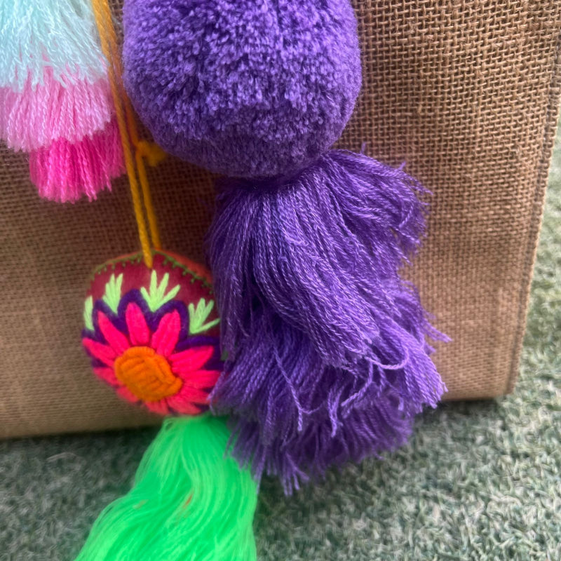 Dark purple fluffy tassel keychain with soft pom pom placed on grass background