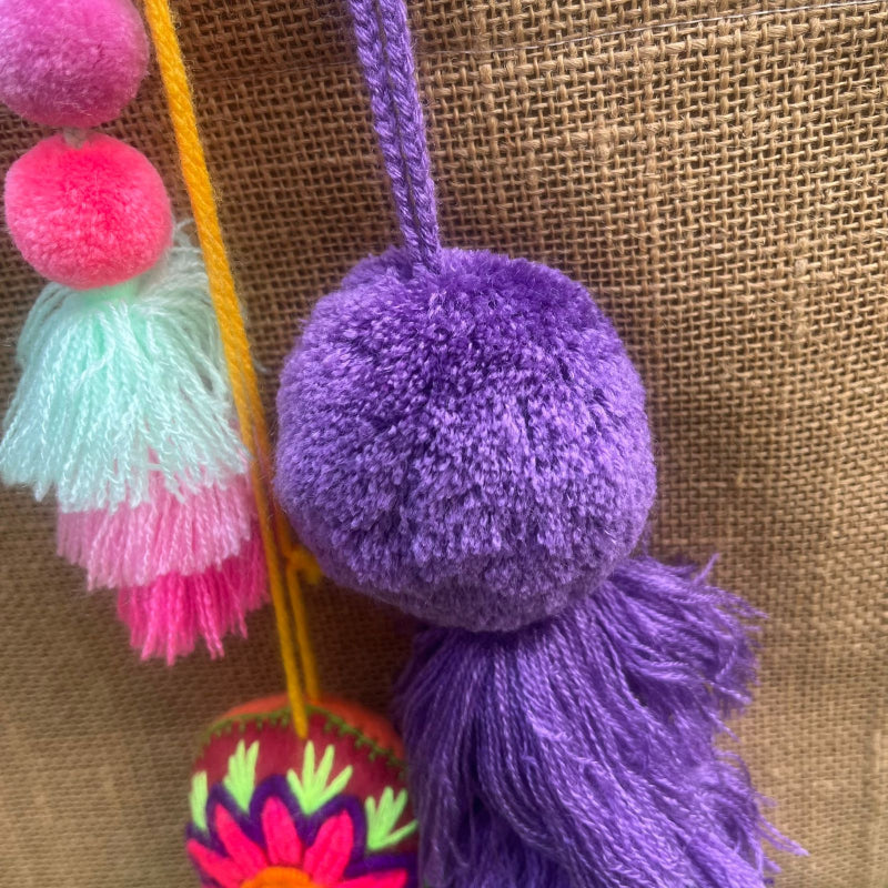 Dark purple fluffy tassel keychain with soft pom pom placed on grass background