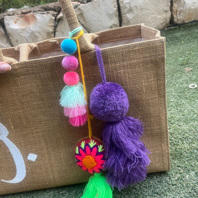 Dark purple fluffy tassel keychain with soft pom pom placed on grass background