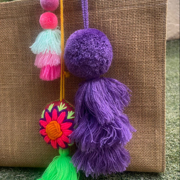 Dark purple fluffy tassel keychain with soft pom pom placed on grass background