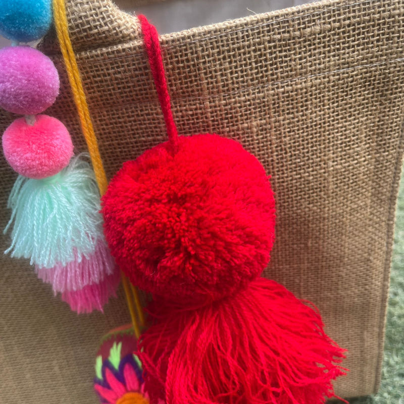 Red fluffy tassel keychain with soft pom pom placed on grass background