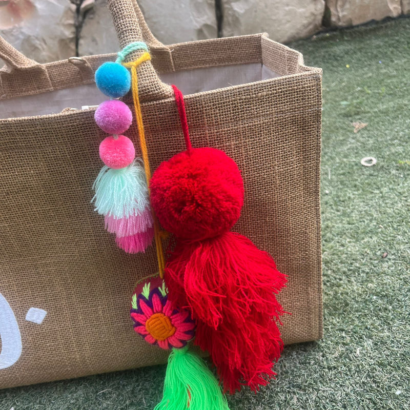 Red fluffy tassel keychain with soft pom pom placed on grass background