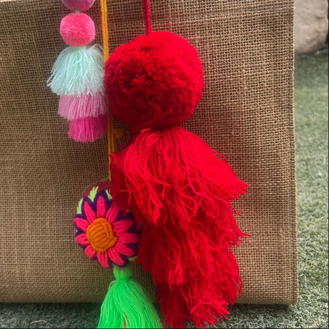 Red fluffy tassel keychain with soft pom pom placed on grass background