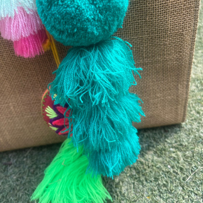 Green fluffy tassel keychain with soft pom pom placed on grass background