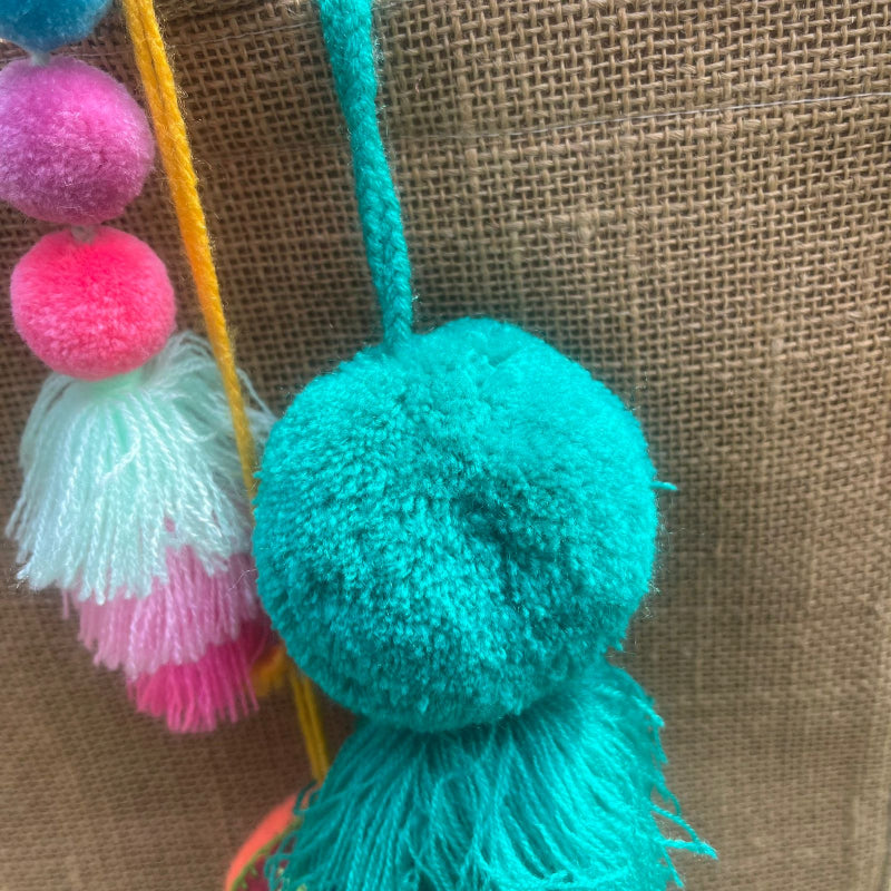 Green fluffy tassel keychain with soft pom pom placed on grass background