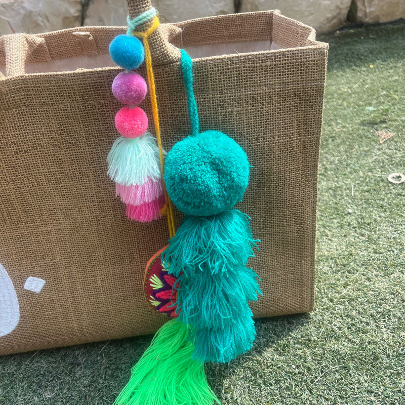 Green fluffy tassel keychain with soft pom pom placed on grass background