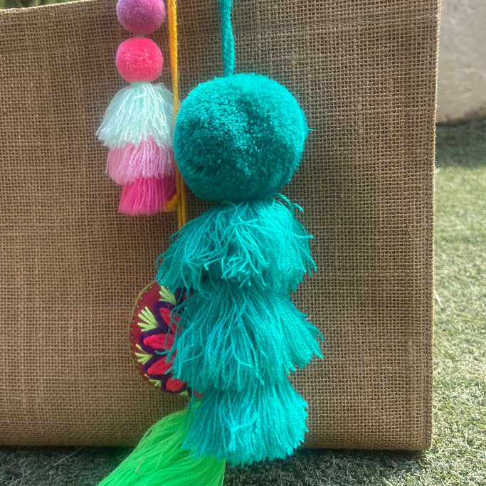 Green fluffy tassel keychain with soft pom pom placed on grass background