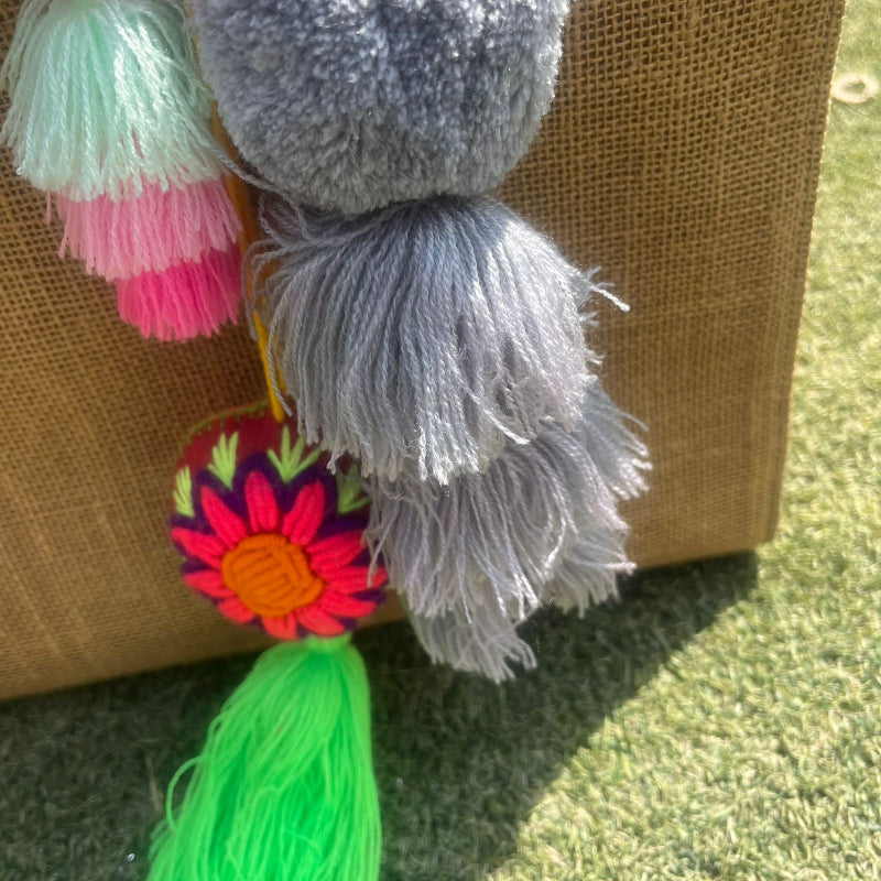 Grey fluffy tassel keychain with soft pom pom placed on grass background