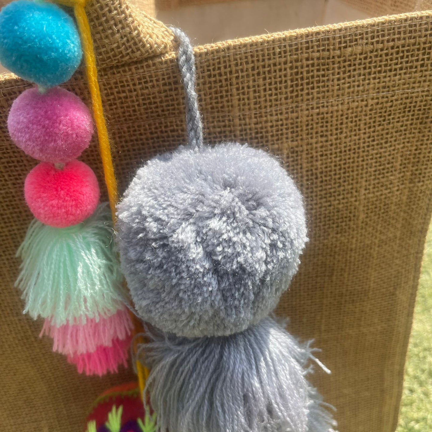 Grey fluffy tassel keychain with soft pom pom placed on grass background