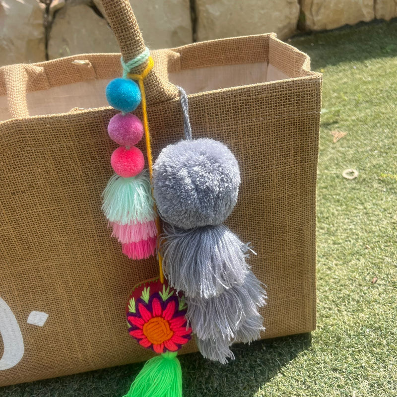 Grey fluffy tassel keychain with soft pom pom placed on grass background