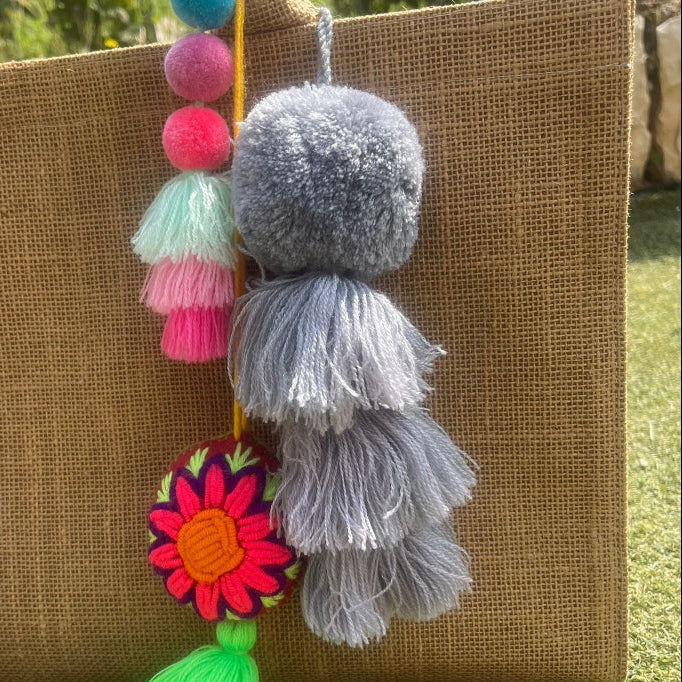 Grey fluffy tassel keychain with soft pom pom placed on grass background