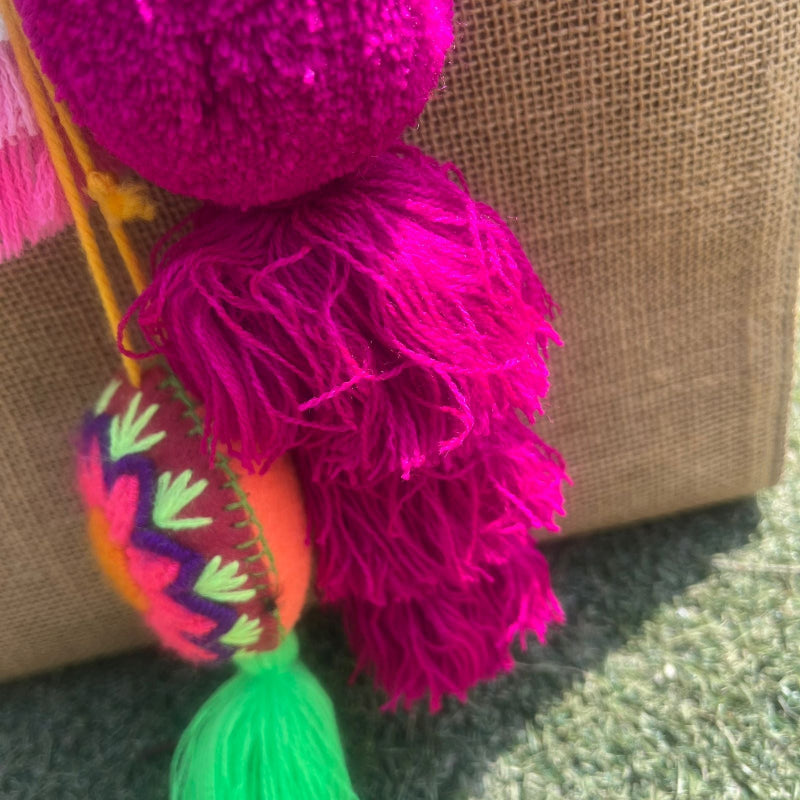 Fuchsia fluffy tassel keychain with soft pom pom placed on grass background