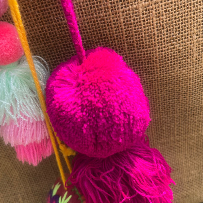 Fuchsia fluffy tassel keychain with soft pom pom placed on grass background
