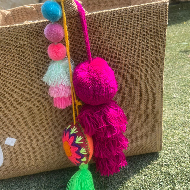 Fuchsia fluffy tassel keychain with soft pom pom placed on grass background