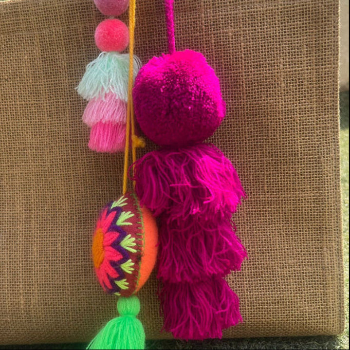 Fuchsia fluffy tassel keychain with soft pom pom placed on grass background