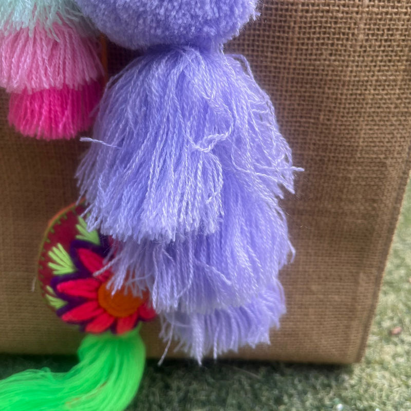 Purple fluffy tassel keychain with soft pom pom placed on grass background
