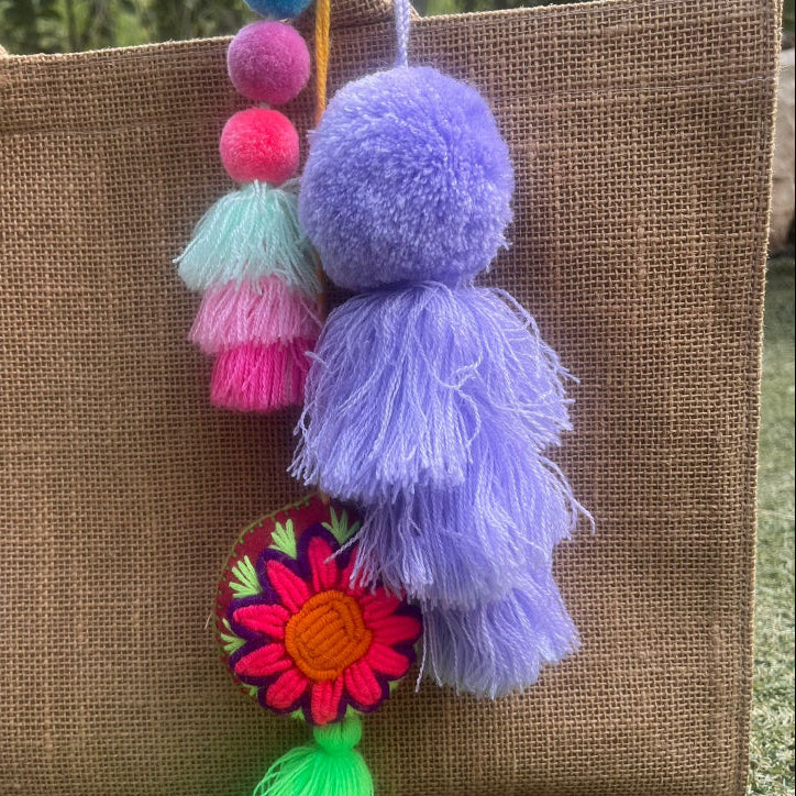 Purple fluffy tassel keychain with soft pom pom placed on grass background