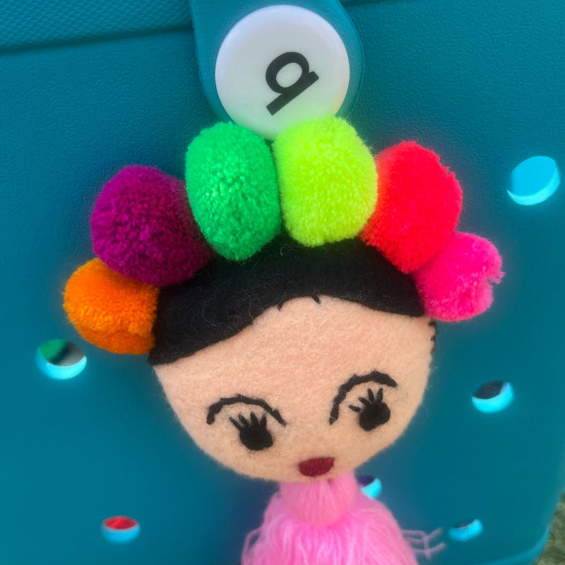 Handmade Frida-inspired doll charm with colorful pom-poms and soft pink tassel on teal bag
