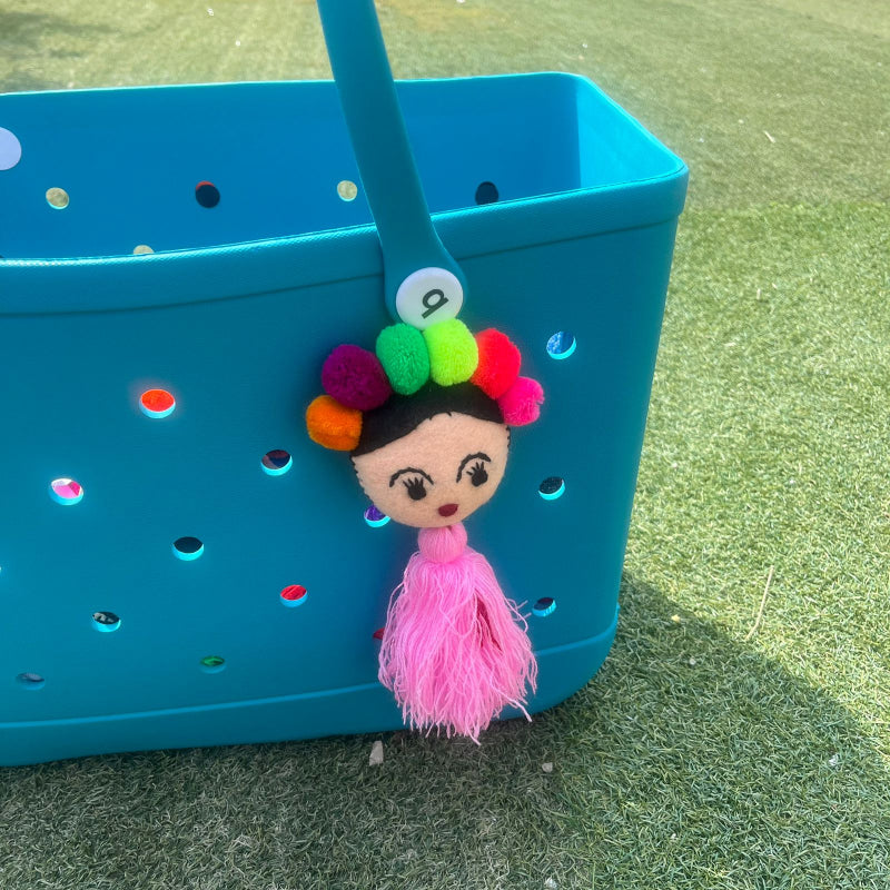 Handmade Frida-inspired doll charm with colorful pom-poms and soft pink tassel on teal bag