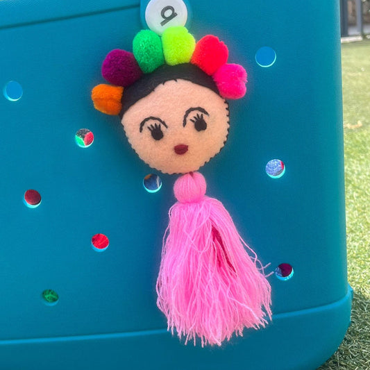 Handmade Frida-inspired doll charm with colorful pom-poms and soft pink tassel on teal bag