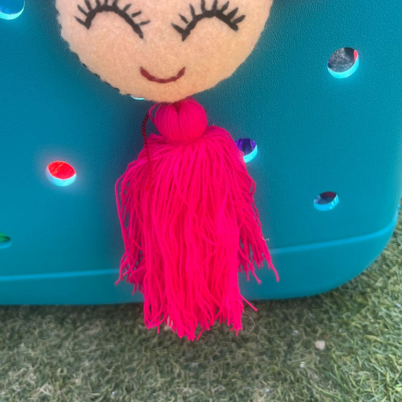 Handmade smiling Frida-inspired doll charm with colorful pom-poms and pink tassel on teal bag