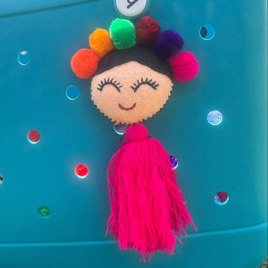 Handmade smiling Frida-inspired doll charm with colorful pom-poms and pink tassel on teal bag