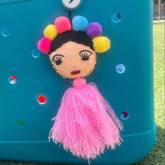 Handmade Frida-inspired doll charm with colorful pom-poms and light pink tassel on teal bag