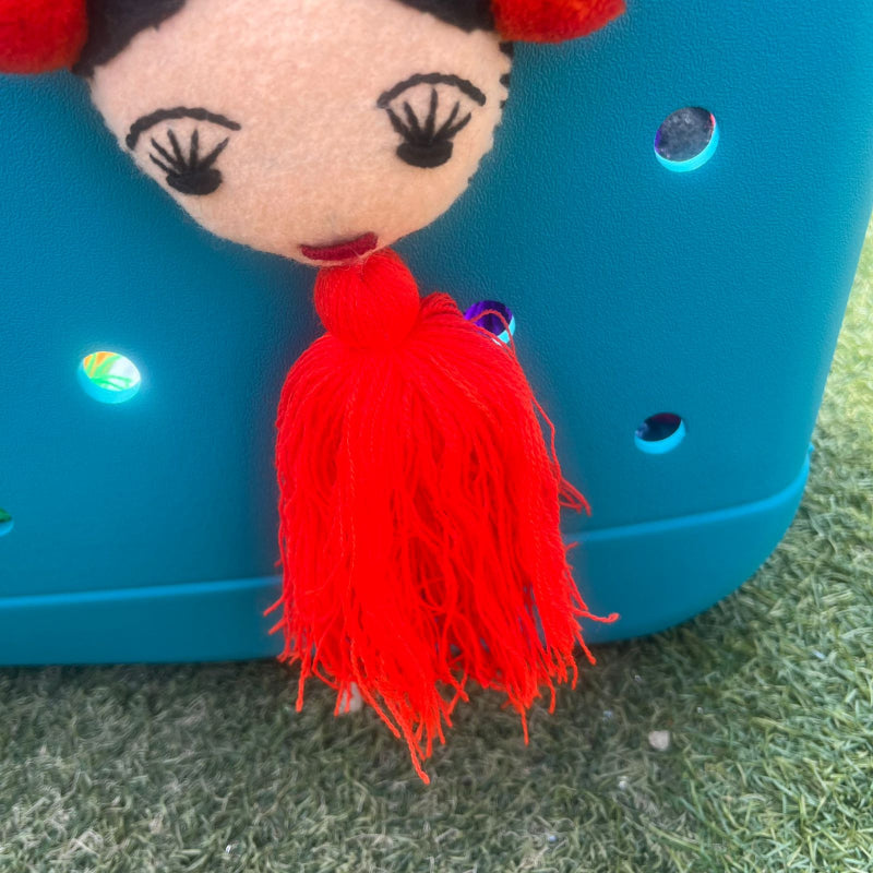 Handmade Frida-inspired doll charm with red pom-poms and red tassel on teal bag