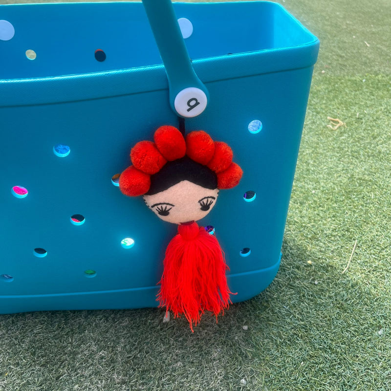 Handmade Frida-inspired doll charm with red pom-poms and red tassel on teal bag