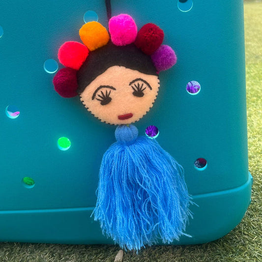 Handmade Frida-inspired doll ornament with colorful pom-poms and blue tassel attached to teal bag