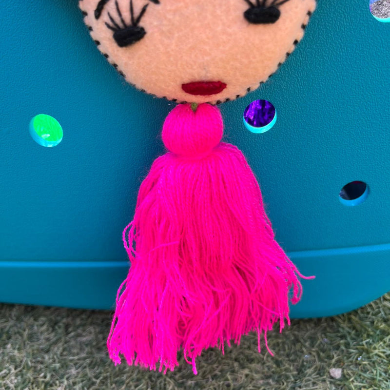 Handmade Frida-inspired doll charm with colorful pom-poms and pink tassel on teal bag