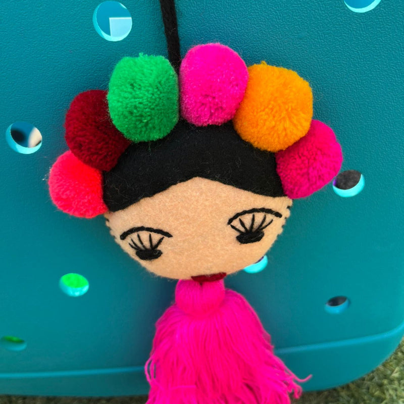 Handmade Frida-inspired doll charm with colorful pom-poms and pink tassel on teal bag