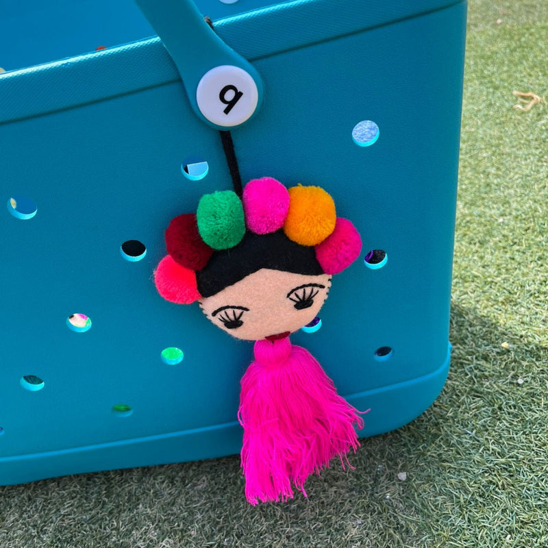 Handmade Frida-inspired doll charm with colorful pom-poms and pink tassel on teal bag