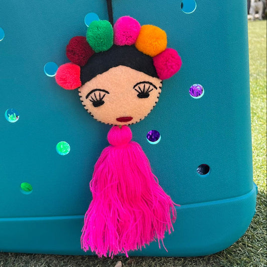 Handmade Frida-inspired doll charm with colorful pom-poms and pink tassel on teal bag