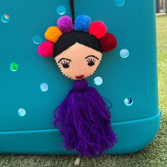 Handmade Frida-inspired doll charm with colorful pom-poms and purple tassel attached to teal bag