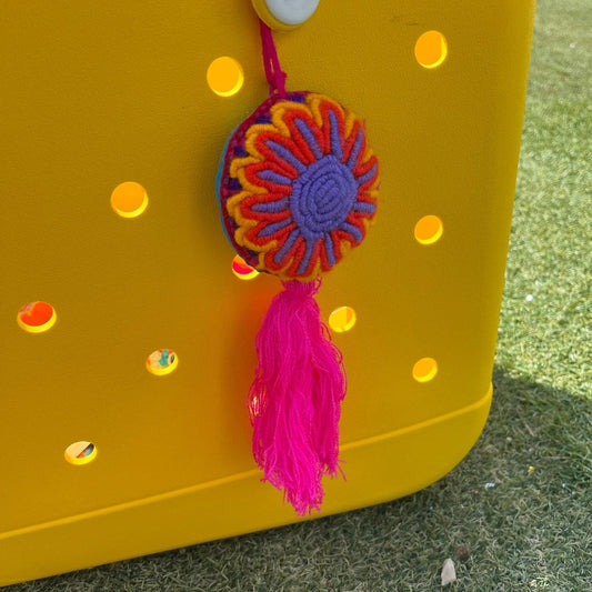 Handmade vibrant embroidered floral ornament with multicolor design and pink tassel on yellow background