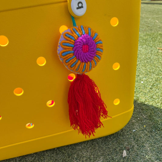Handmade colorful embroidered floral ornament with orange and blue details and red tassel on yellow background