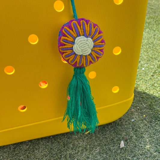 Handmade multicolor embroidered floral ornament with yellow and purple petals and green tassel on yellow background