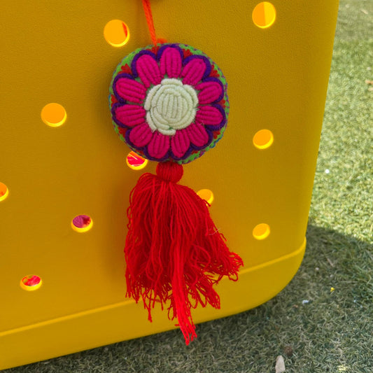 Handmade pink embroidered floral ornament with cream center and red tassel hanging on yellow background