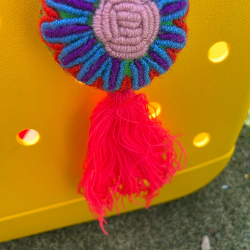 Handmade multicolor embroidered flower ornament with pastel center and red tassel on a yellow background