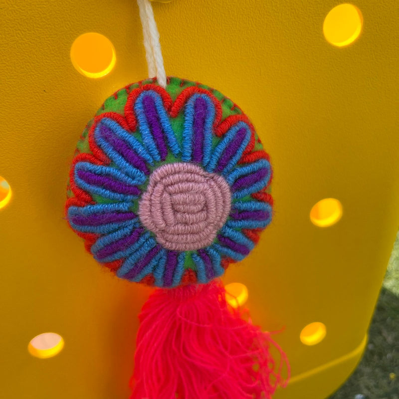 Handmade multicolor embroidered flower ornament with pastel center and red tassel on a yellow background